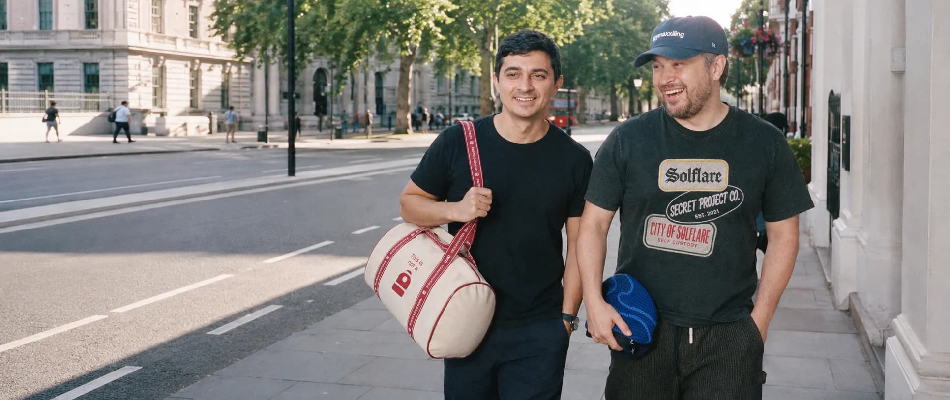 Two people wearing custom-made apparel and carrying a branded duffel on a London street